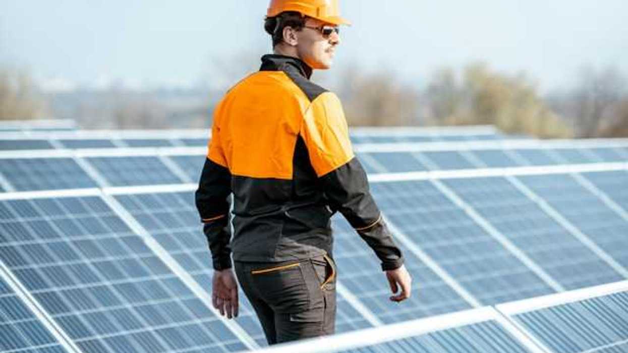 A worker in an orange hard hat inspecting solar polars