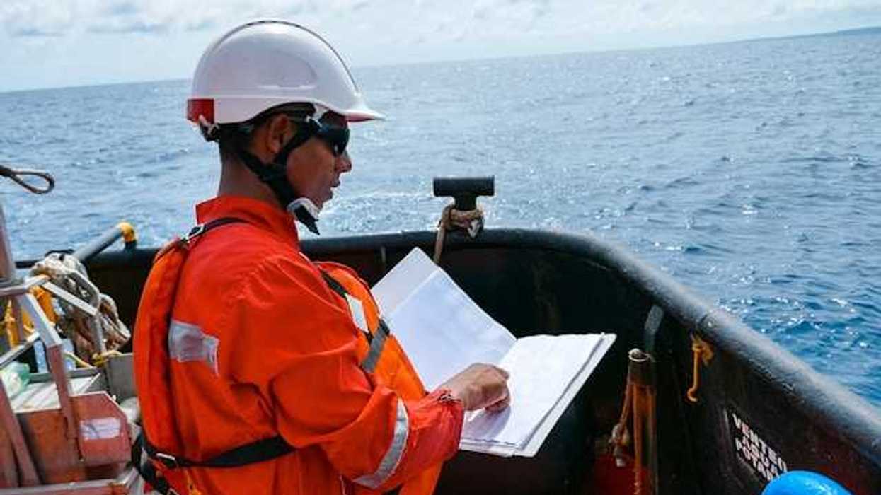 A worker in an orange jumpsuit and hardhat on an oil drill
