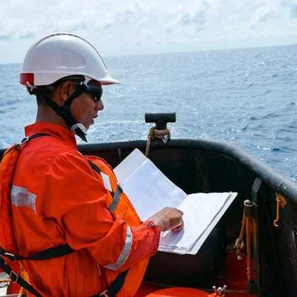 A worker in an orange jumpsuit and hardhat on an oil drill