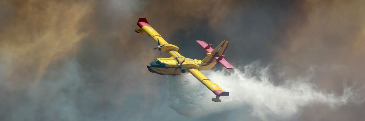 A yellow airplane dropping water on a wildfire surrounded by smoke.