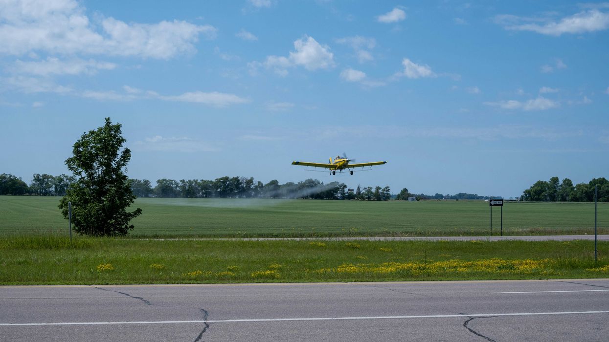 a yellow plane flying over a field spraying pesticides