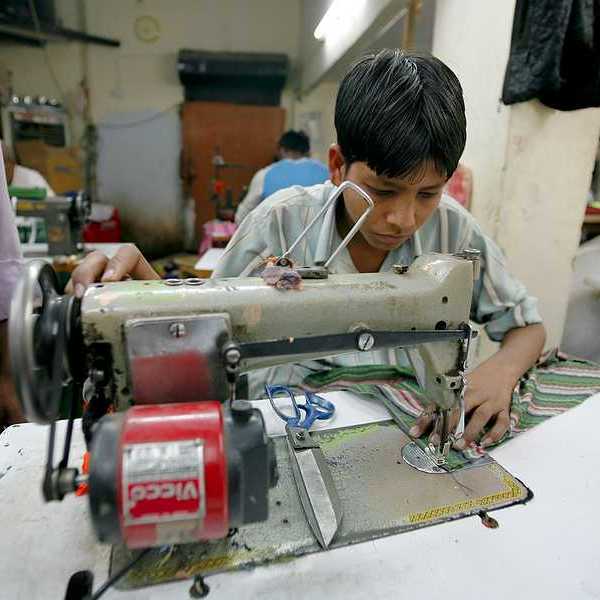 A young Asian boy sitting at a sewing machine in a factory