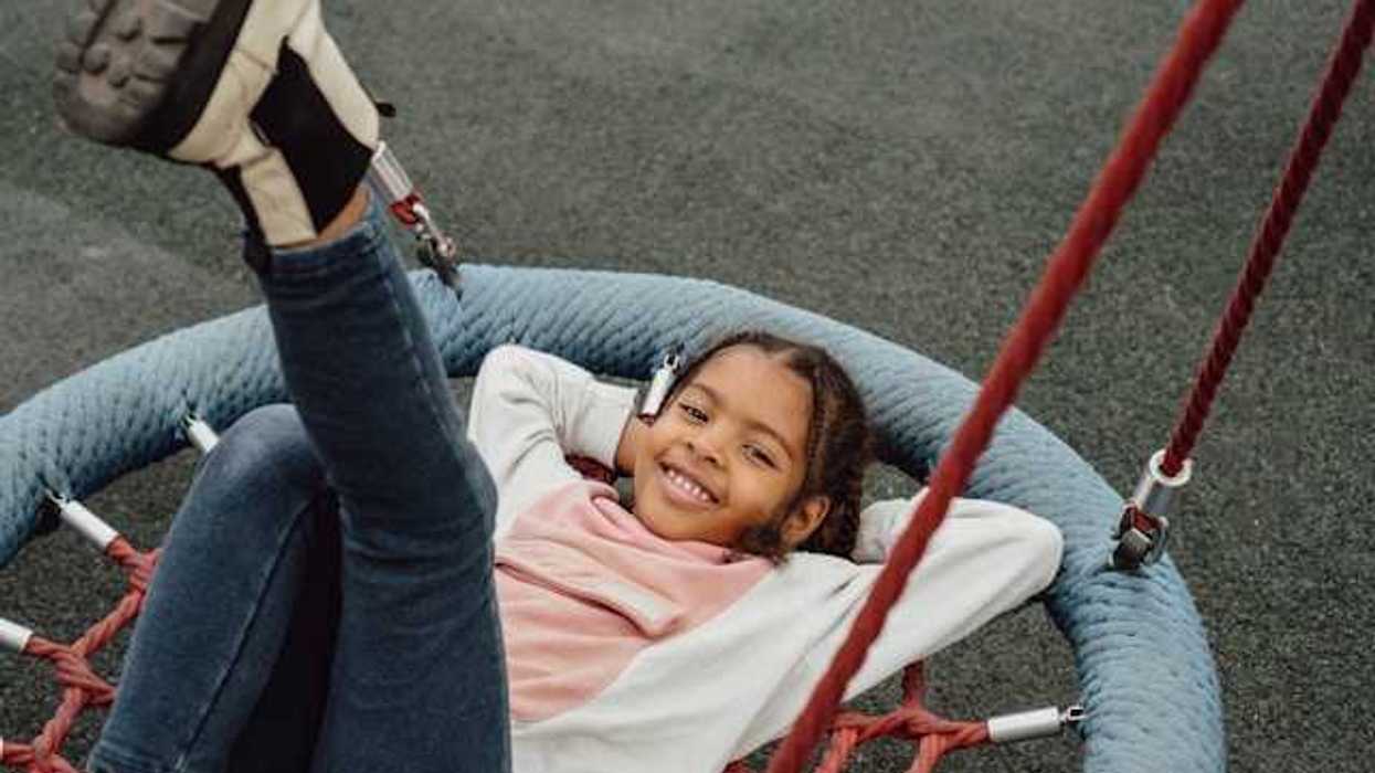 A young Black girl playing on a playground swing