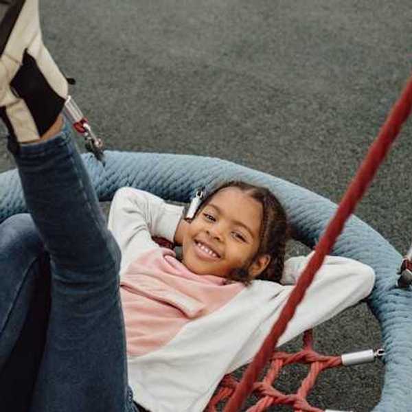 A young Black girl playing on a playground swing