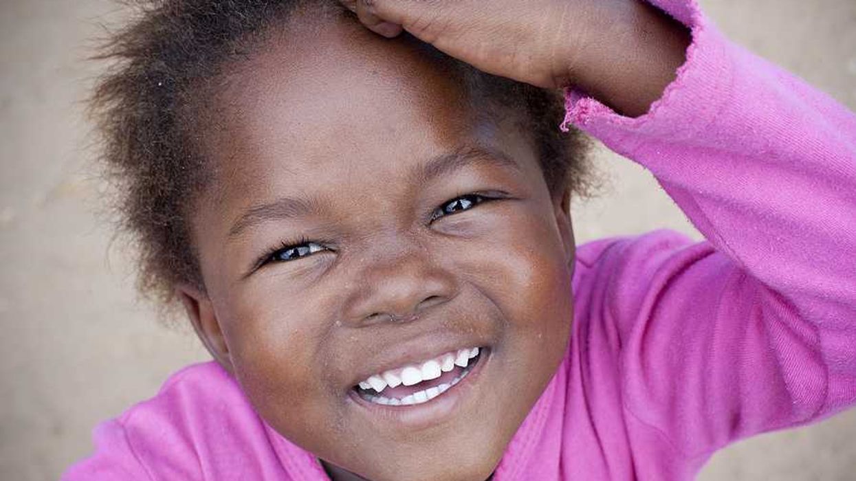 A young Black toddler wearing a pink shirt and looking into the camera