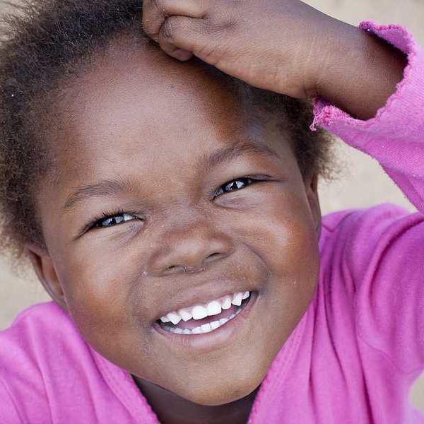 A young Black toddler wearing a pink shirt and looking into the camera
