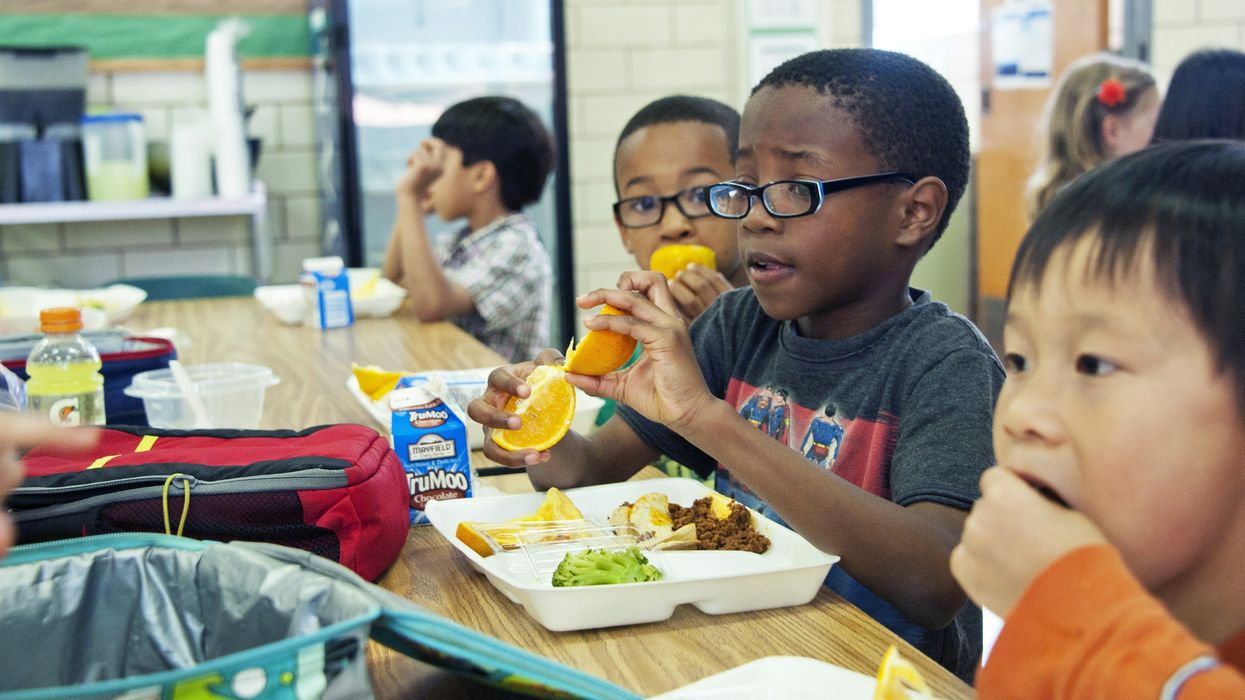 A young boy eats school lunch out of a disposable tray.