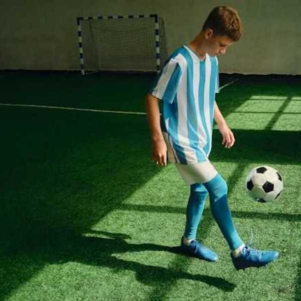 A young boy kicking a soccer ball on an artificial turf surface