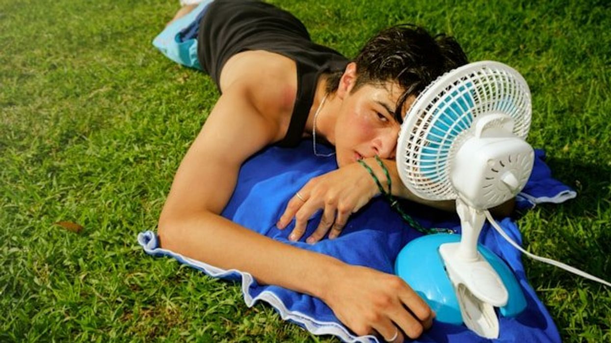 A young man lying on the grass with a portable fan on a hot day.