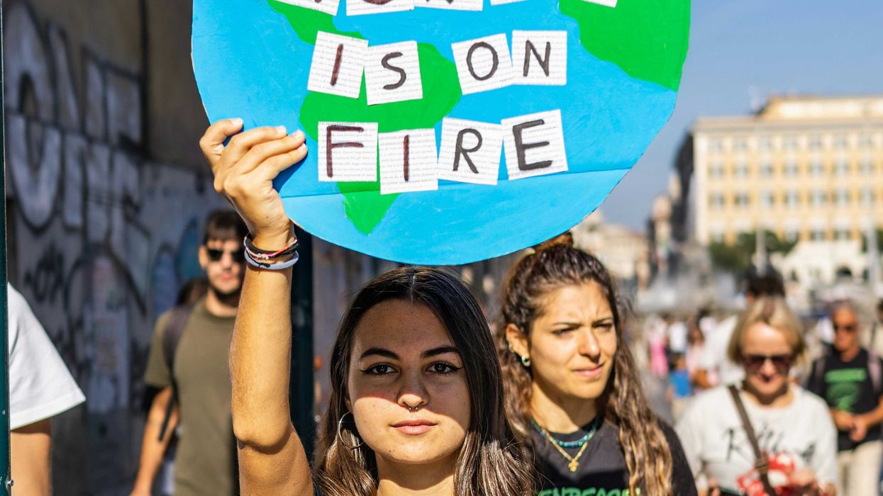 a young woman at a climate protest holding a sign that says this world is on fire.