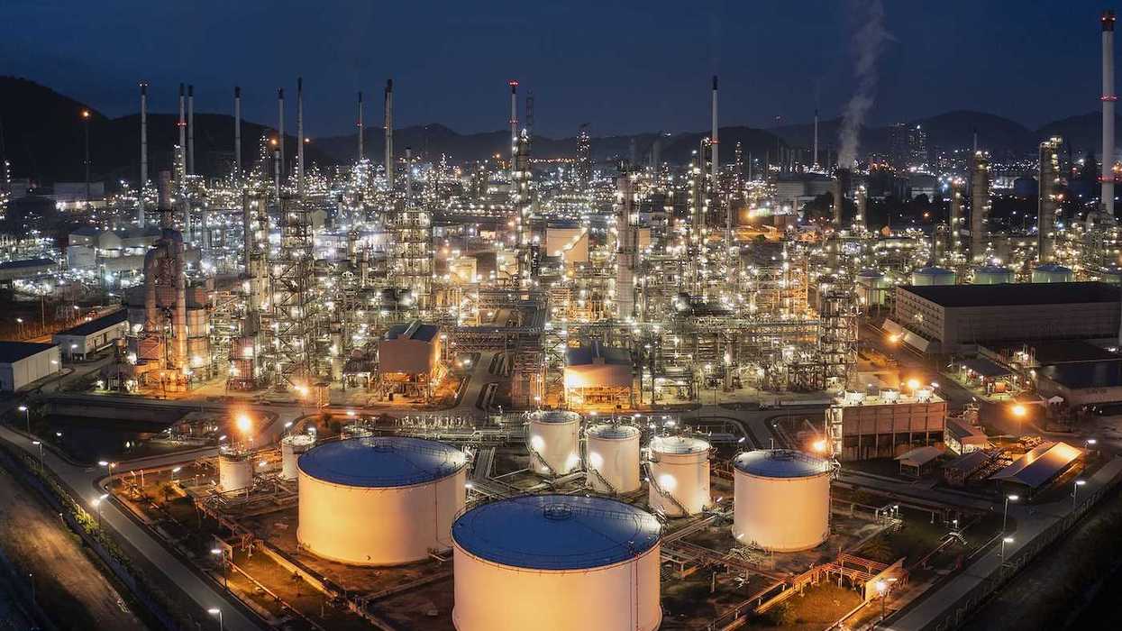 Aerial drone view of oil storage tanks in foreground with oil refinery behind.
