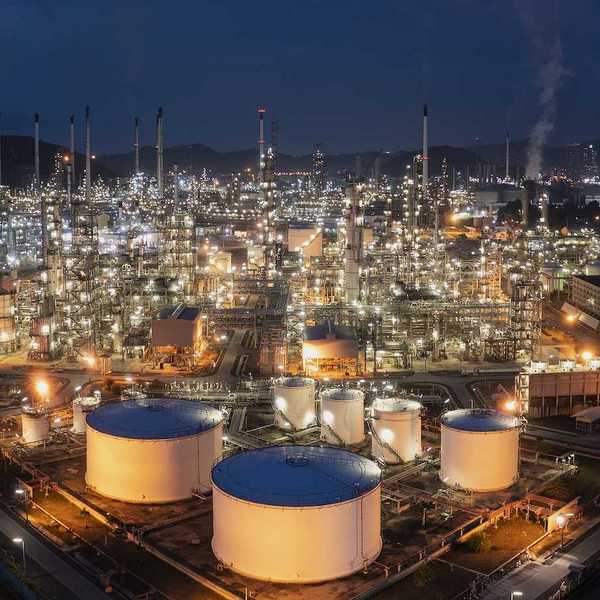 Aerial drone view of oil storage tanks in foreground with oil refinery behind.
