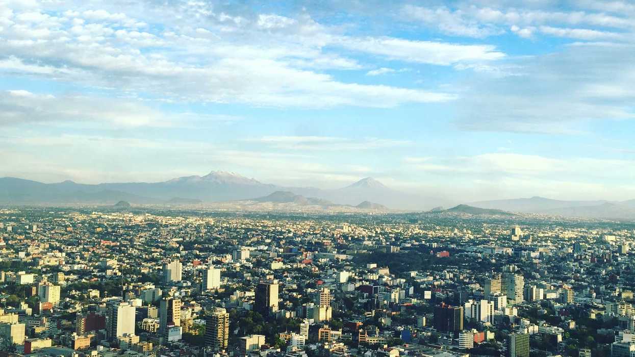 aerial photo of cityscape under white clouds at daytime with mountains in distance.
