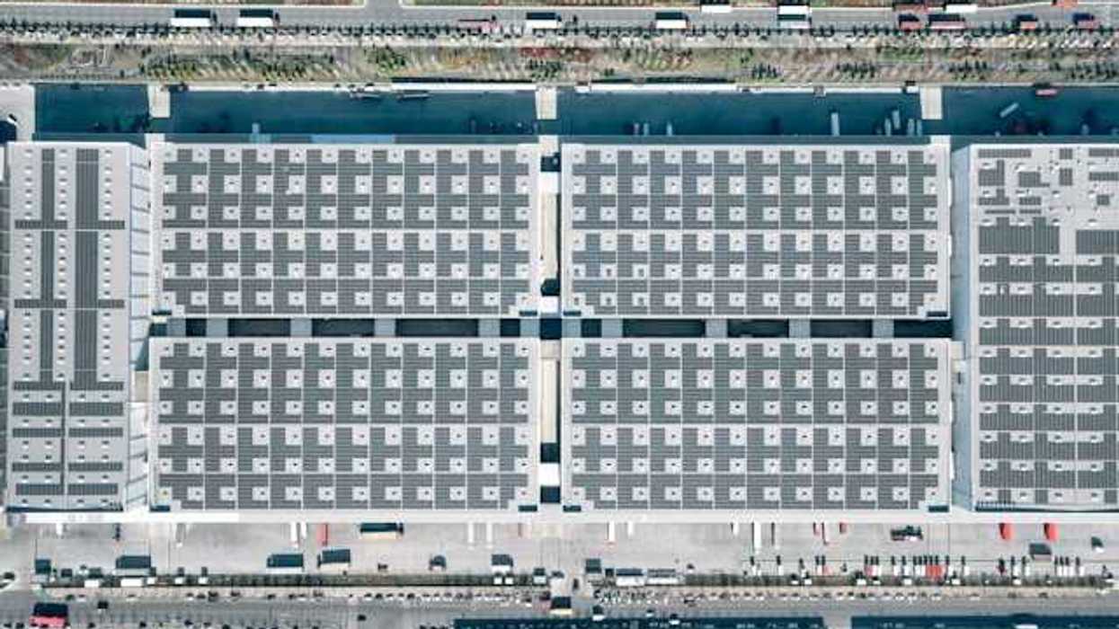 Aerial view of a city building with solar panels covering it and roads with cars on either side