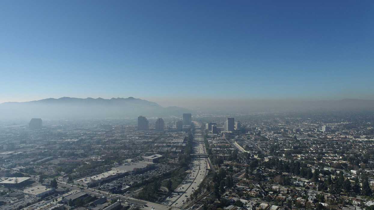 Aerial view of a city shrouded in smog criss-crossed by freeways with mountains in background.