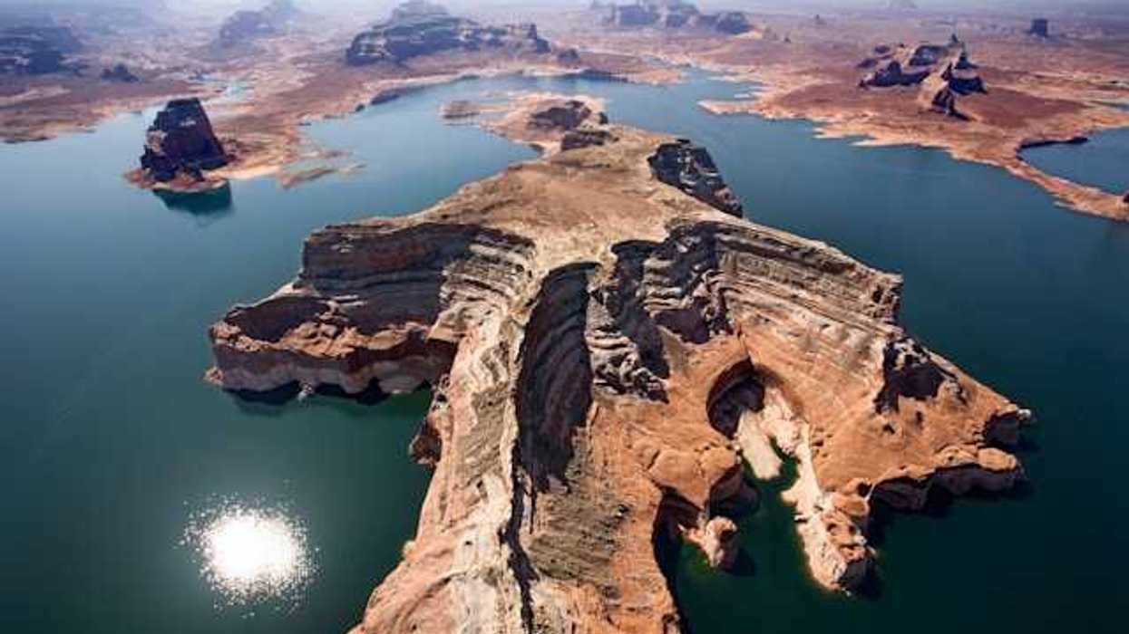 Aerial view of a lake with reddish rock formations in the center and perimeter of it