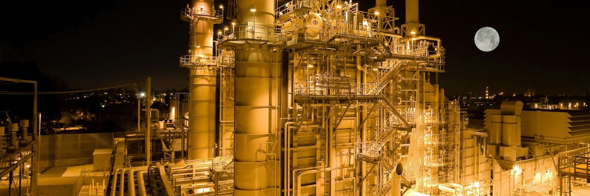 Aerial view of a refinery lit up at night with a full moon in the background.