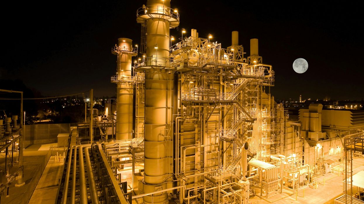 Aerial view of a refinery lit up at night with a full moon in the background.