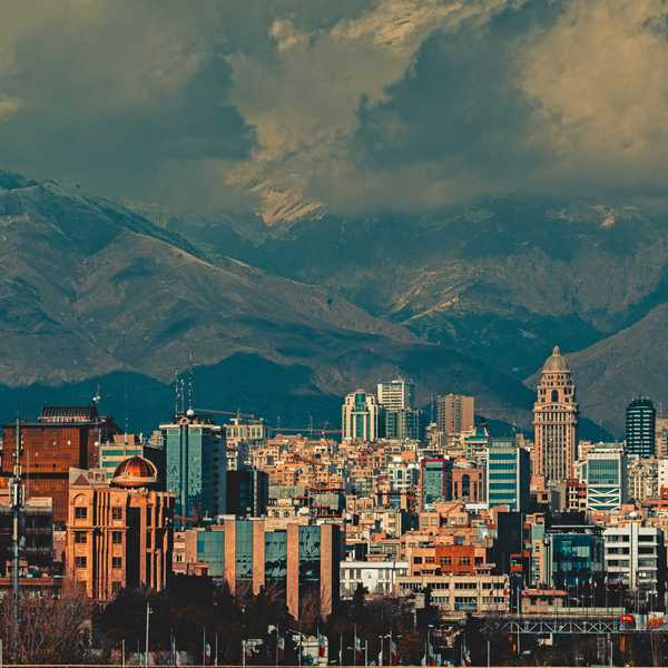 aerial view of city buildings during daytime with large mountains and clouds in background.