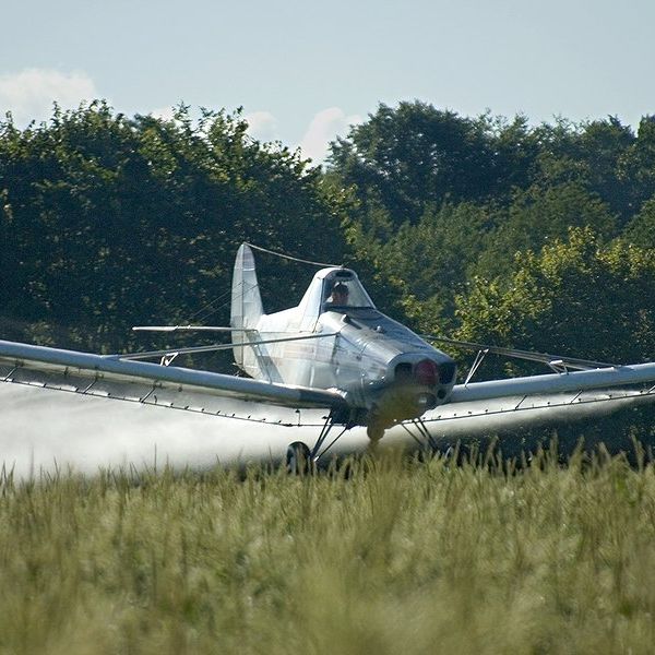 Airplane dropping pesticide or herbicide on a field.