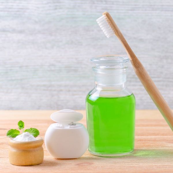 alternative natural mmouthwash bottle with toothpaste xylitol or soda or salt and wood toothbrush dental floss on wooden background