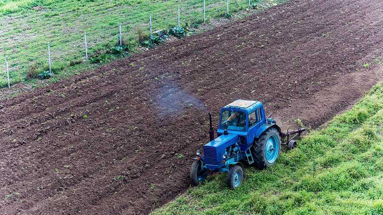 An aerial view of a blue tractor applying brown fertilizer to a green field