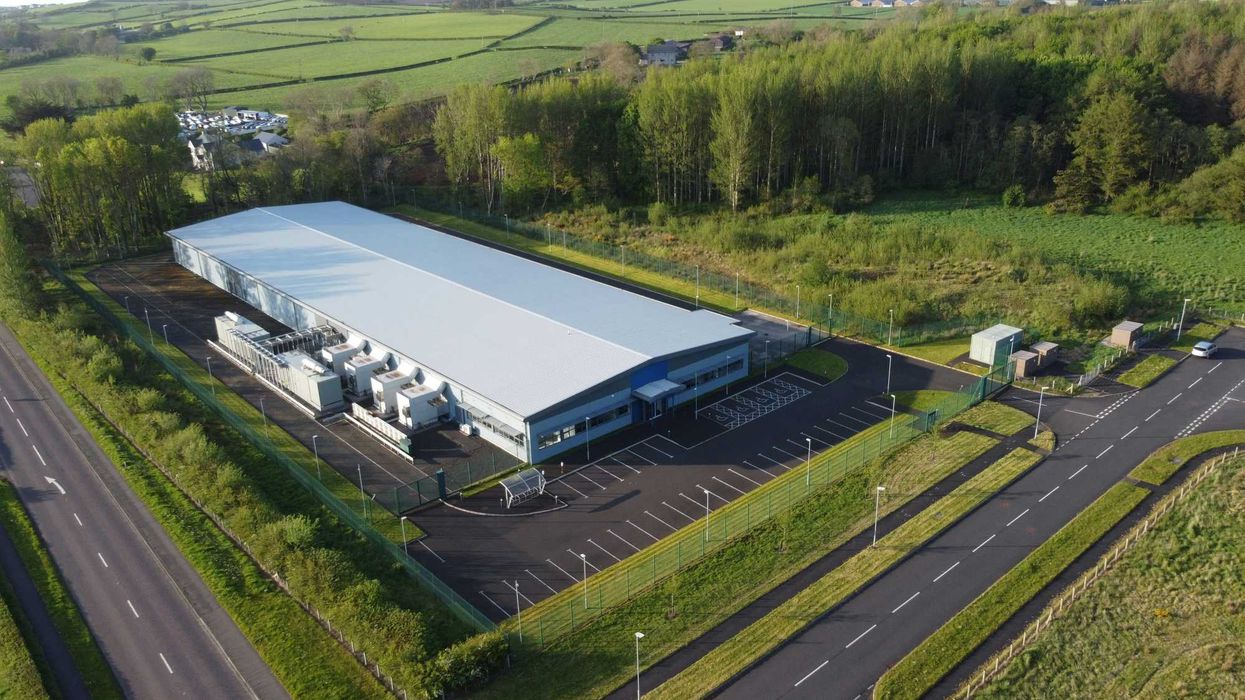 an aerial view of a data center flanked by trees, roads and green fields.