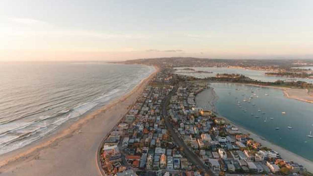 An aerial view of a peninsula with ocean on one side and a harbor on the other with houses on the land