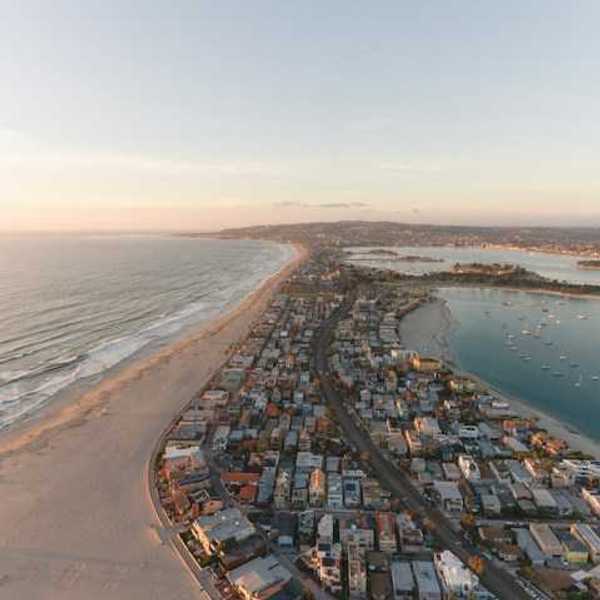 An aerial view of a peninsula with ocean on one side and a harbor on the other with houses on the land