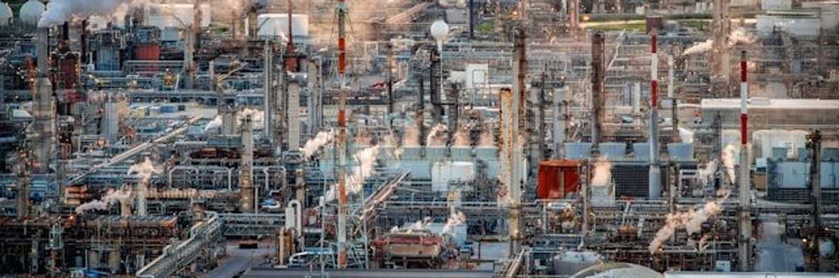 An aerial view of a refinery with a city in the background.