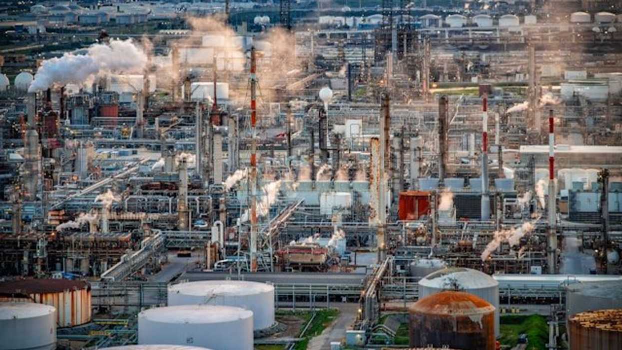 An aerial view of a refinery with a city in the background.