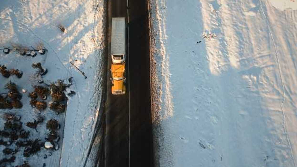 An aerial view of a semi truck on a road in a snowy landscape