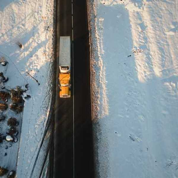 An aerial view of a semi truck on a road in a snowy landscape