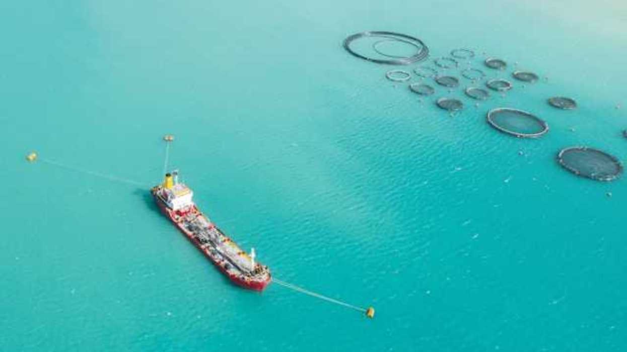 An aerial view of a ship sitting next to round fish holding tanks in the ocean
