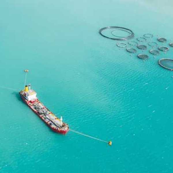 An aerial view of a ship sitting next to round fish holding tanks in the ocean