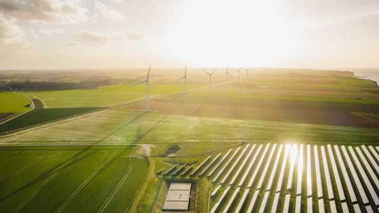 An aerial view of a solar farm with wind turbines in the background