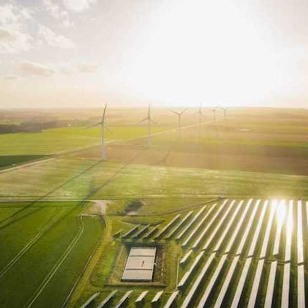 An aerial view of a solar farm with wind turbines in the background