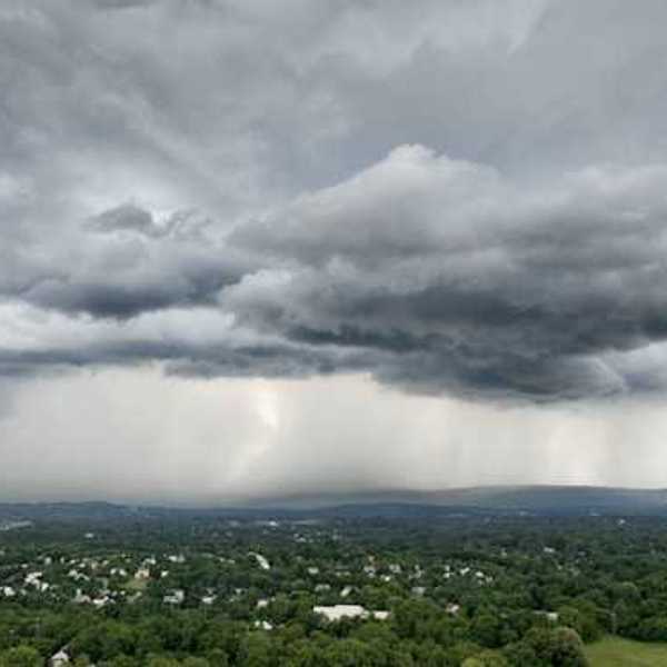 An aerial view of a town surrounded by green trees with a huge storm in the distance