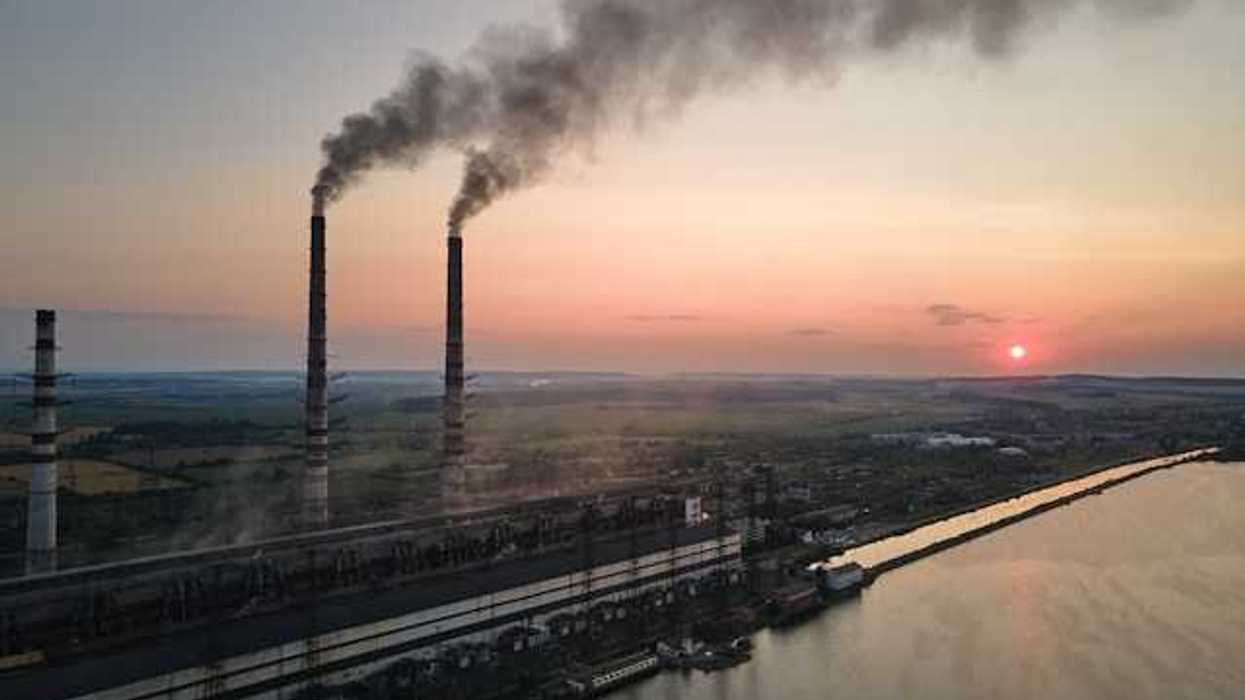 An aerial view of three smokestacks emitting smoke into the air with the setting sun in the background