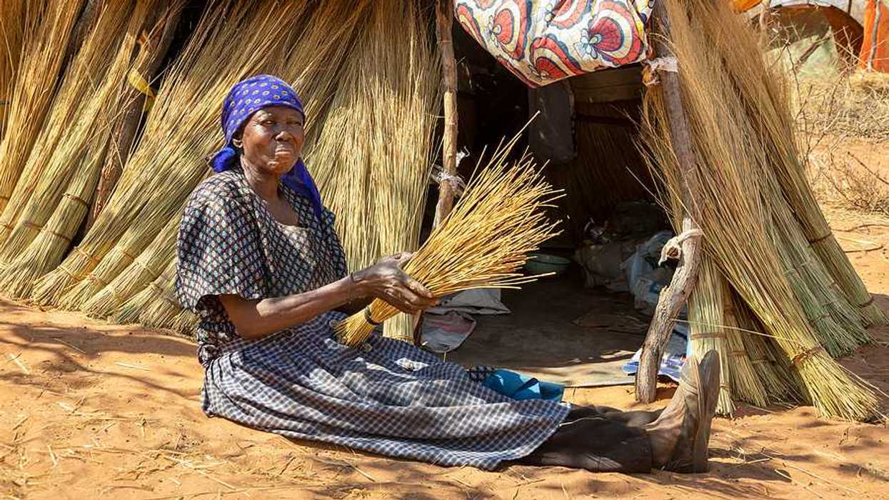 An African woman sitting on the ground in front of a thatched hut