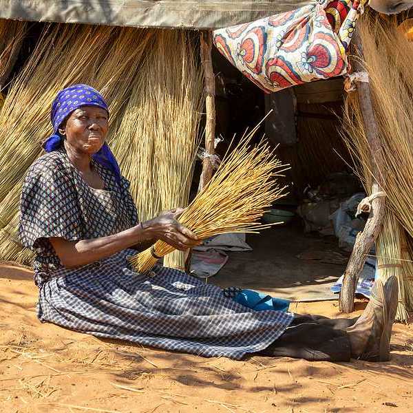An African woman sitting on the ground in front of a thatched hut