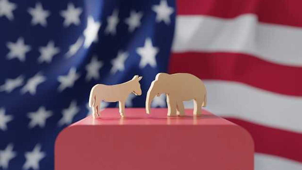 An American flag with wooden cutouts of a donkey and an elephant in the foreground