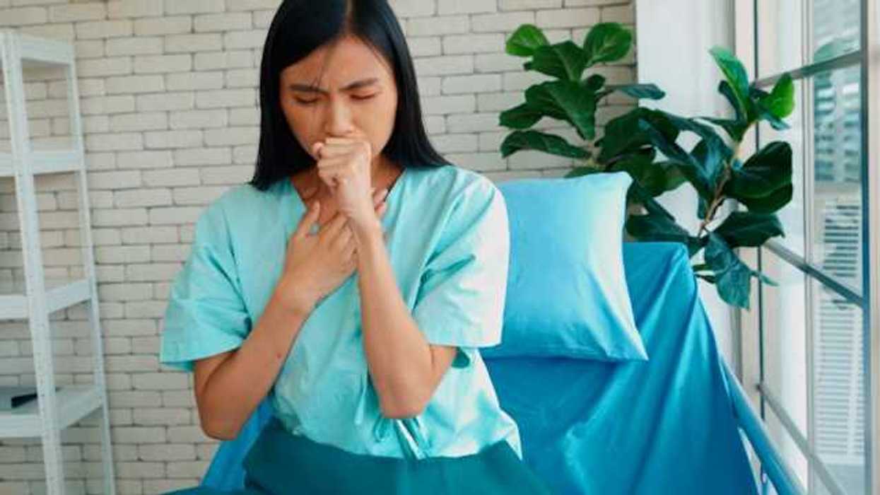 An Asian woman sitting on a bed and coughing