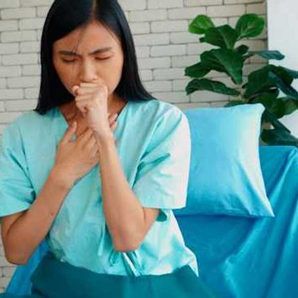 An Asian woman sitting on a bed and coughing