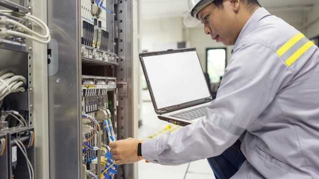 An Asian worker kneeling in front of a server with a laptop
