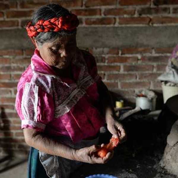 An elderly Guatemalan woman peeling a tomato in a rustic kitchen