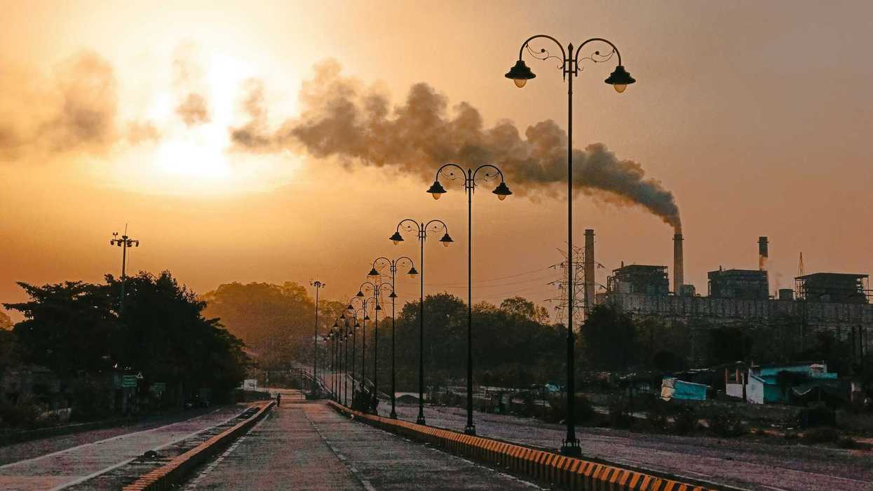 An empty street with a smokestack in background releasing pollution into an orange-colored sky.