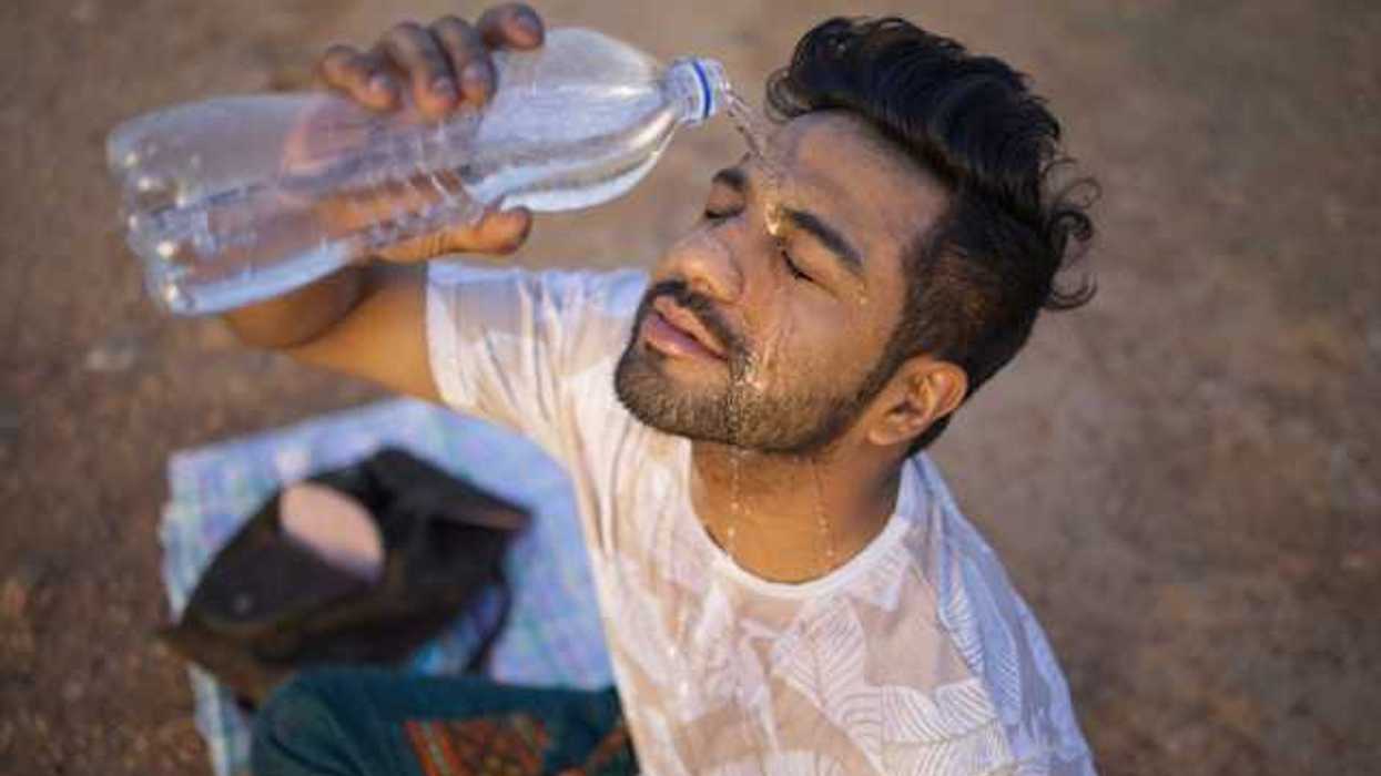 An Indian man sitting on the ground pouring a bottle of water on his face on a hot day