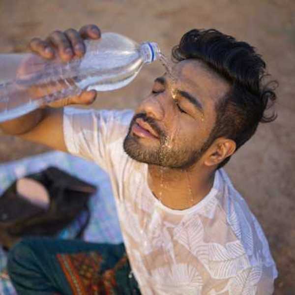 An Indian man sitting on the ground pouring a bottle of water on his face on a hot day