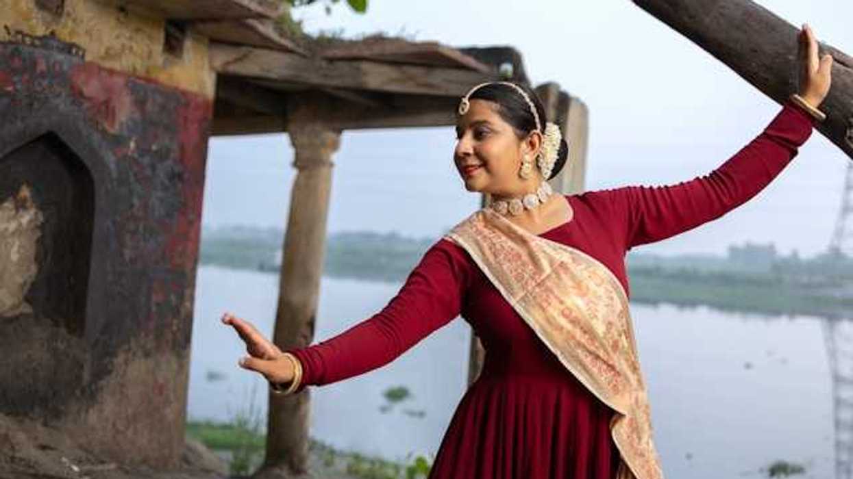An Indian woman wearing jewerly and a sash dancing next to a river